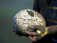 Leriga händer som håller i lerig rugbyboll